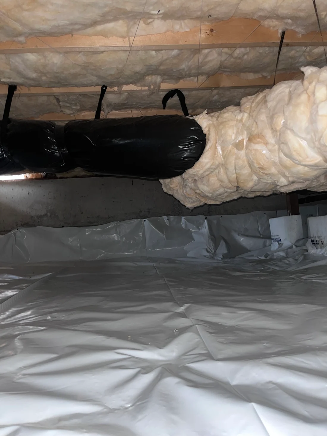 Finished crawlspace with a clean white vapor barrier across the floor, ceiling insulation, and ductwork